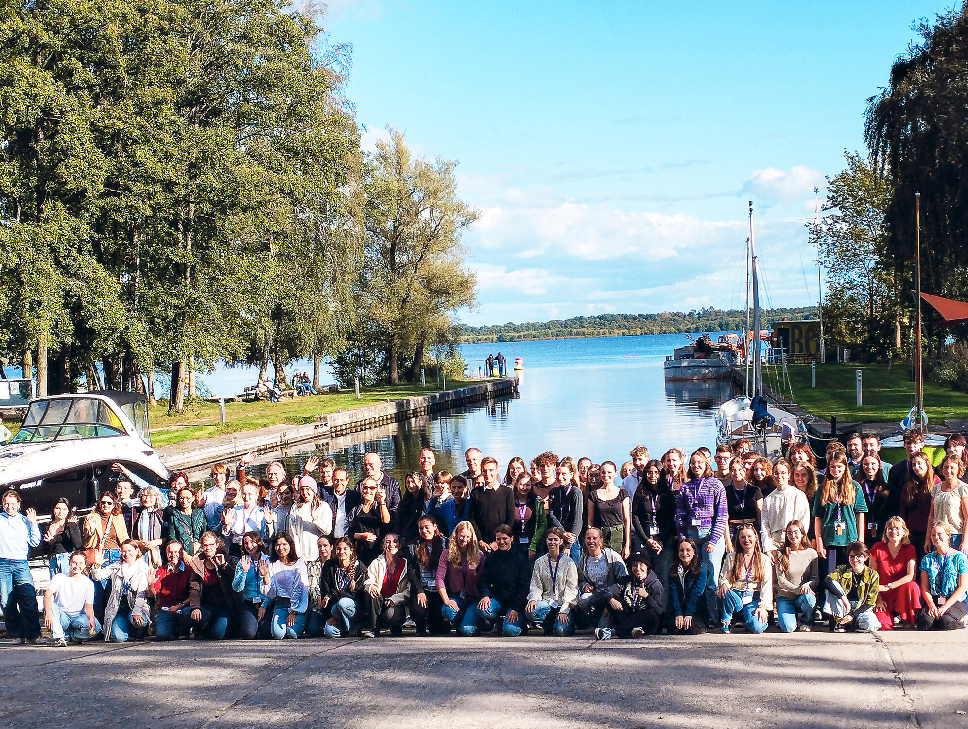 Gruppenfoto mit Teilnehmenden des Sprachenturniers. Im Hintergrund sieht man einen See und ein Segelboot. 